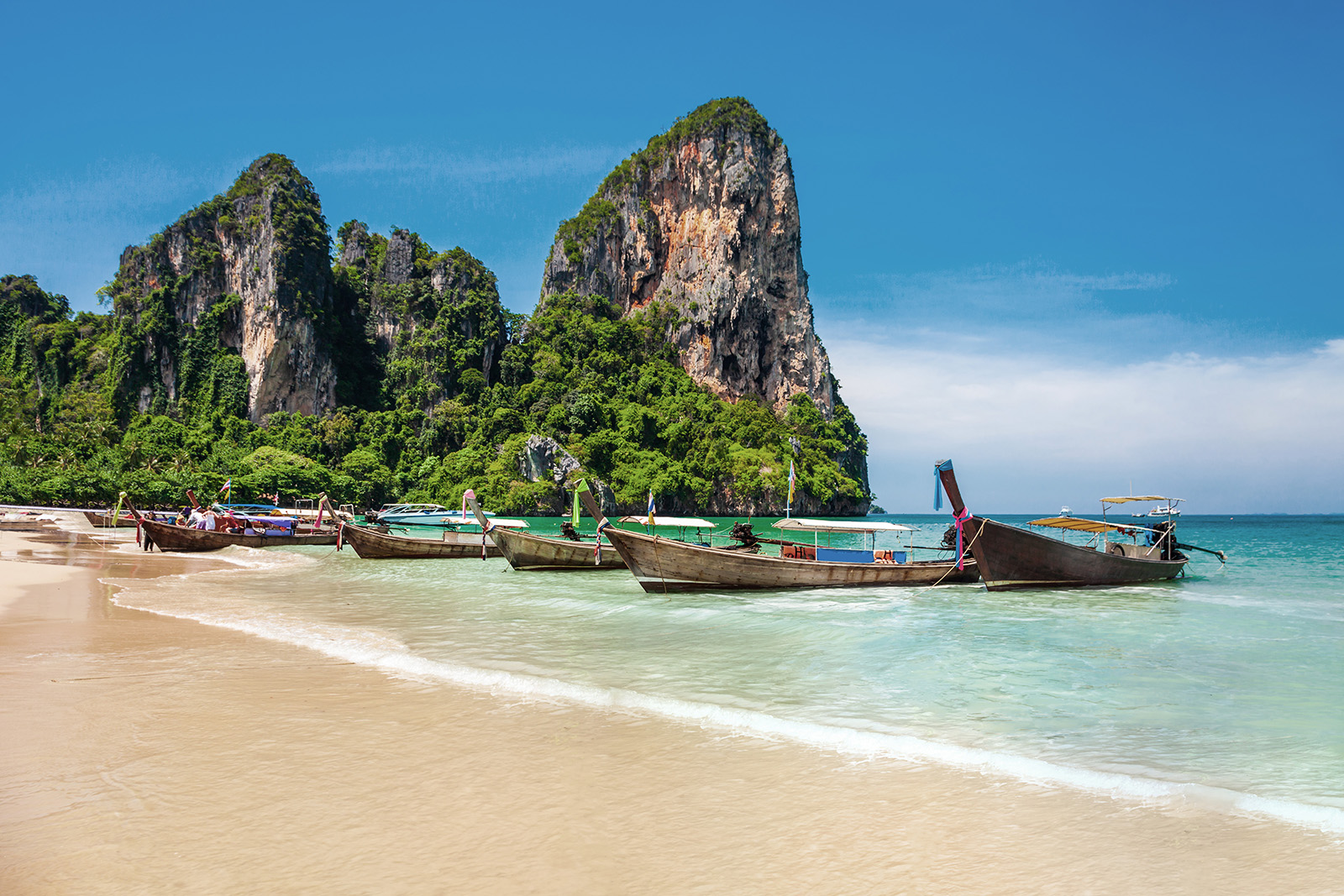 Strand in Thailand mit Booten, Felsen und kristallklarem Wasser, Pauschalreise nach Thailand